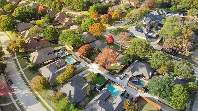 An aerial view of a suburban neighborhood featuring houses with swimming pools nestled among mature trees during the autumn season.