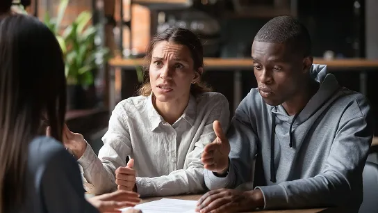 A woman and a man sitting at a table having a serious conversation with a professional, likely a lawyer or consultant.