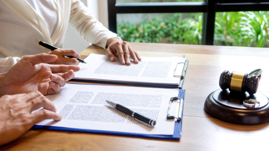 A client and her attorney sign papers at a desk.