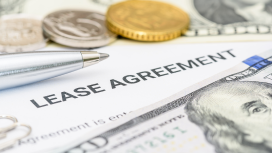 Property rental, leasing contracts, real estate, housing agreements, and property management. A close-up view of a lease agreement document with paperclips, coins, US dollar, and a pen placed on top.